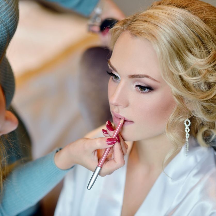 A woman getting her lips painted by a makeup artist.